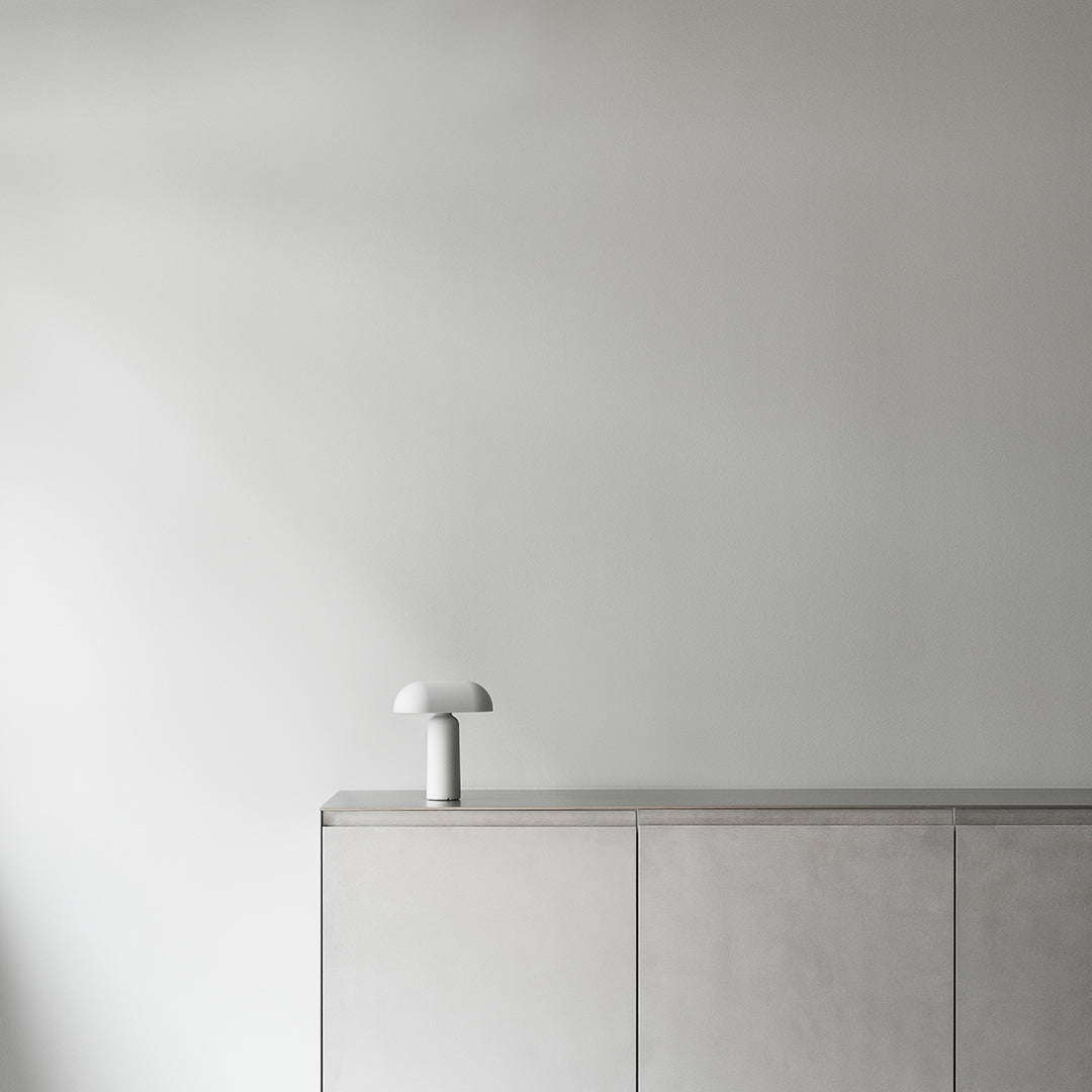 Minimalist white lamp on a smooth gray cabinet against a softly lit, neutral wall. Contemporary and sleek design.