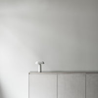 Minimalist white lamp on a smooth gray cabinet against a softly lit, neutral wall. Contemporary and sleek design.