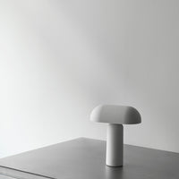 White mushroom-shaped lamp on a sleek gray surface against a minimalist wall for modern decor.