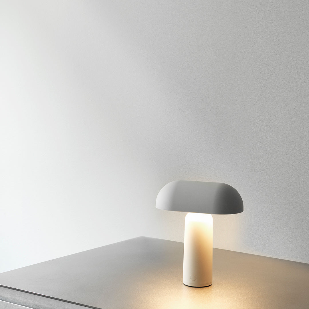 Minimalist white lamp with a smooth, curved shade and a sleek cylindrical base, casting a soft warm glow.