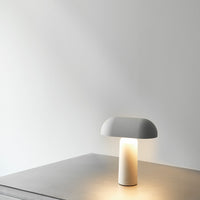 Minimalist white lamp with a smooth, curved shade and a sleek cylindrical base, casting a soft warm glow.