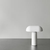 Minimalist white lamp with a smooth, rounded design on a gray surface against a soft gray background.