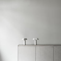 Minimalist gray cabinet with white mushroom lamps on top against a light gray wall, showcasing a sleek, modern aesthetic.