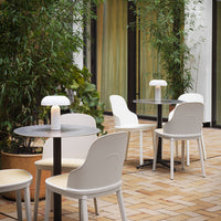 Modern white chairs and black tables set against lush greenery and warm beige tiles, creating a stylish outdoor vibe.