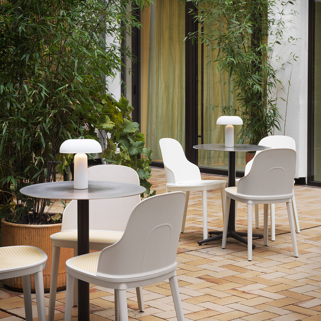 Modern white chairs and black tables set against lush greenery and warm beige tiles, creating a stylish outdoor vibe.