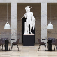 Statuesque white figure on a dark pedestal, surrounded by gray marble walls and stylish brown chairs. Modern decor.