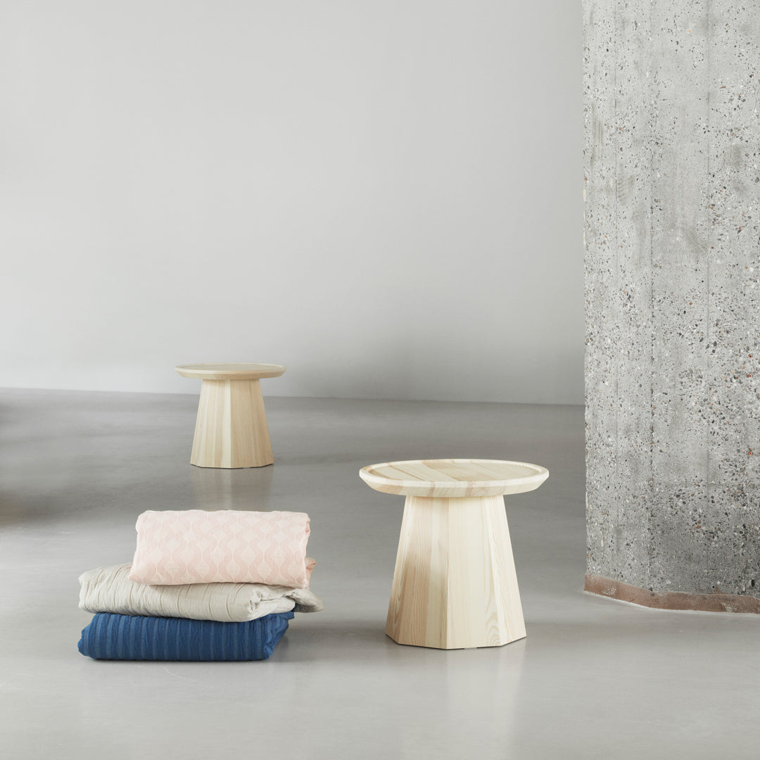 Light beige side tables with textured surfaces beside stacked blankets in soft pink, cream, and navy blue.