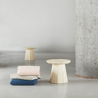 Light beige side tables with textured surfaces beside stacked blankets in soft pink, cream, and navy blue.