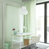 Mint green curtains hang by a large window, paired with a white desk and a gray textured rug, creating a fresh, modern look.
