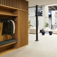 Modern wood display with vertical slats, muted gray floor, and dark fabric coats creating a sophisticated contrast.