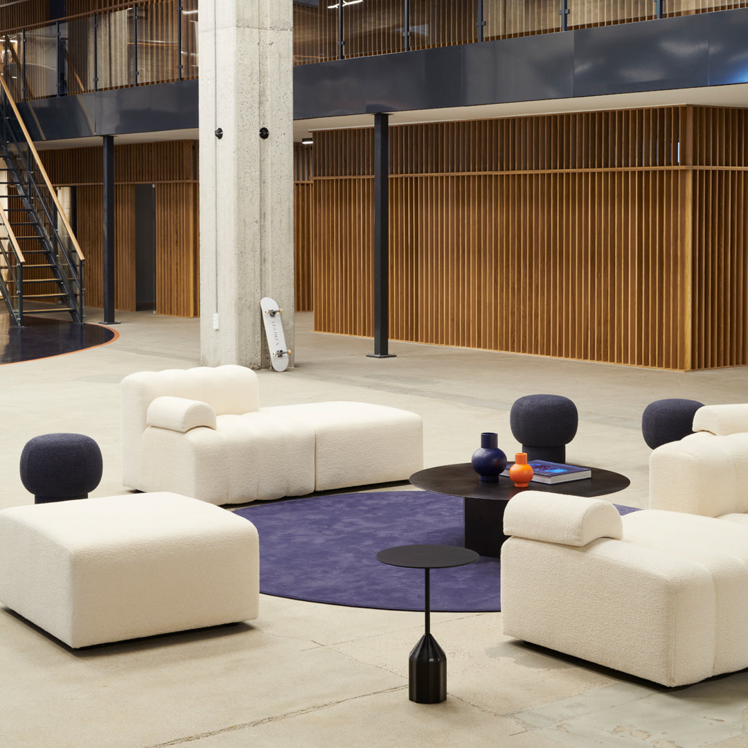 Modern beige furniture set on a rich purple rug, accented with black and colorful decor elements against wood tones.