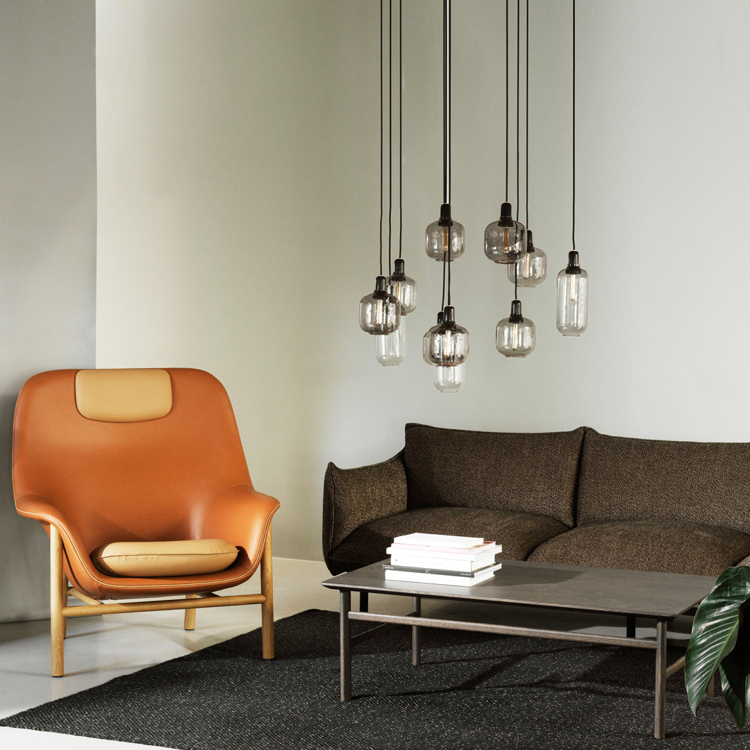 Modern living room featuring a brown sofa, orange accent chair, and sleek black and white decor, with pendant lighting.