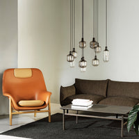 Modern living room featuring a brown sofa, orange accent chair, and sleek black and white decor, with pendant lighting.