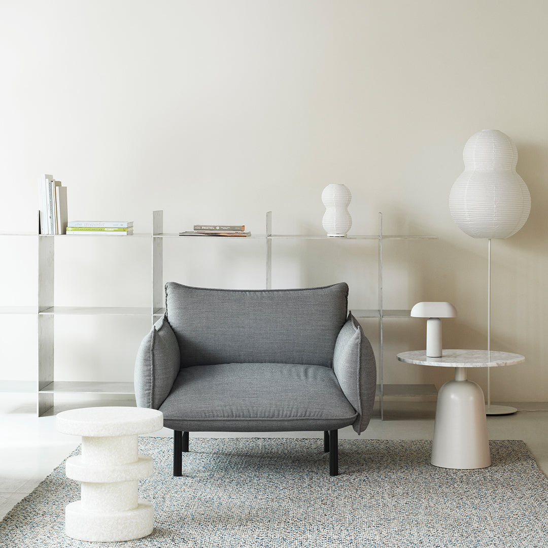 Gray upholstered chair with rounded arms, placed on a textured pale blue and white patterned rug. Light-toned decor.