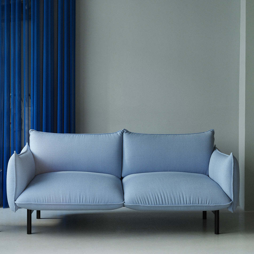 Light blue modern sofa with textured upholstery against a muted wall, complemented by vibrant blue drapes.
