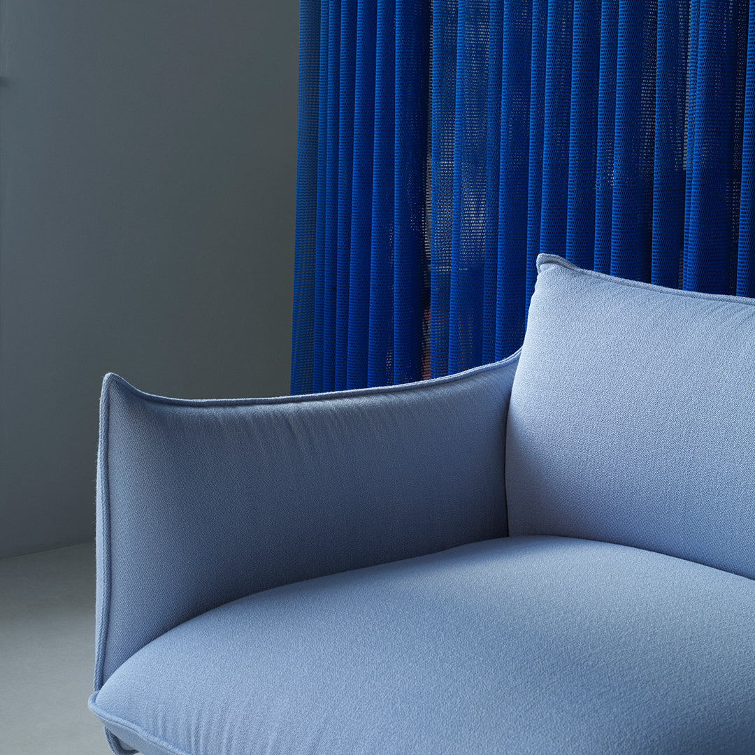 Light blue upholstered sofa with smooth curves, paired with vibrant blue curtain backdrop. Stylish and contemporary design.