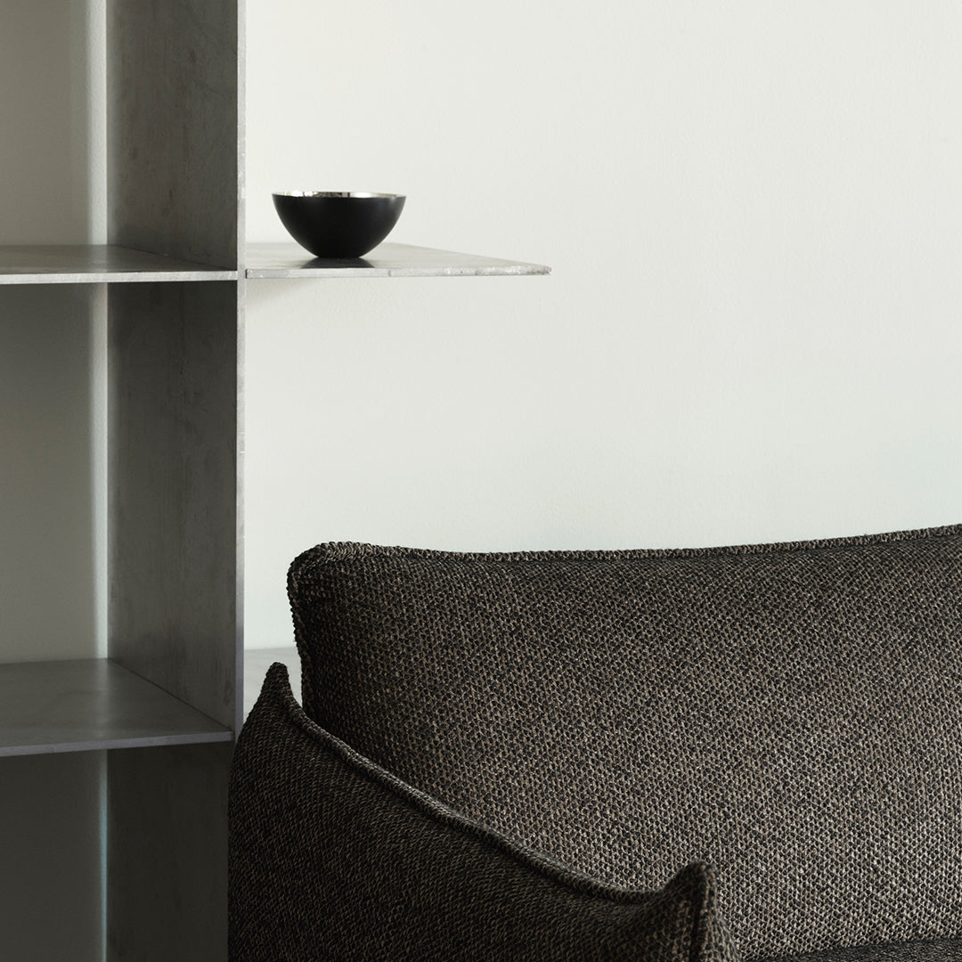 Textured black fabric sofa with subtle patterns, complemented by a minimalist black bowl on a sleek shelf.