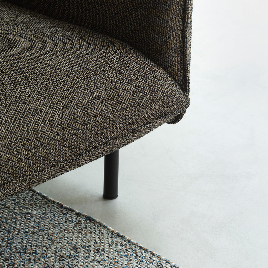 Textured dark brown couch corner with a subtle pattern, paired with a woven multi-colored rug.