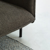 Textured dark brown couch corner with a subtle pattern, paired with a woven multi-colored rug.