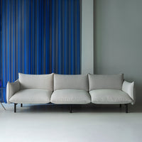 Light gray three-seat sofa with smooth cushions, set against a backdrop of vertical blue stripes.