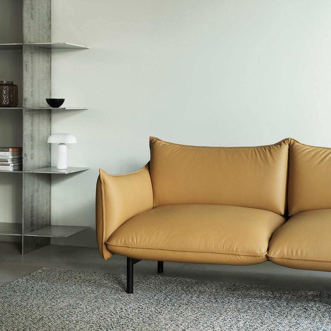 Mustard yellow sofa with smooth upholstery, paired with a textured gray area rug and sleek modern shelving.
