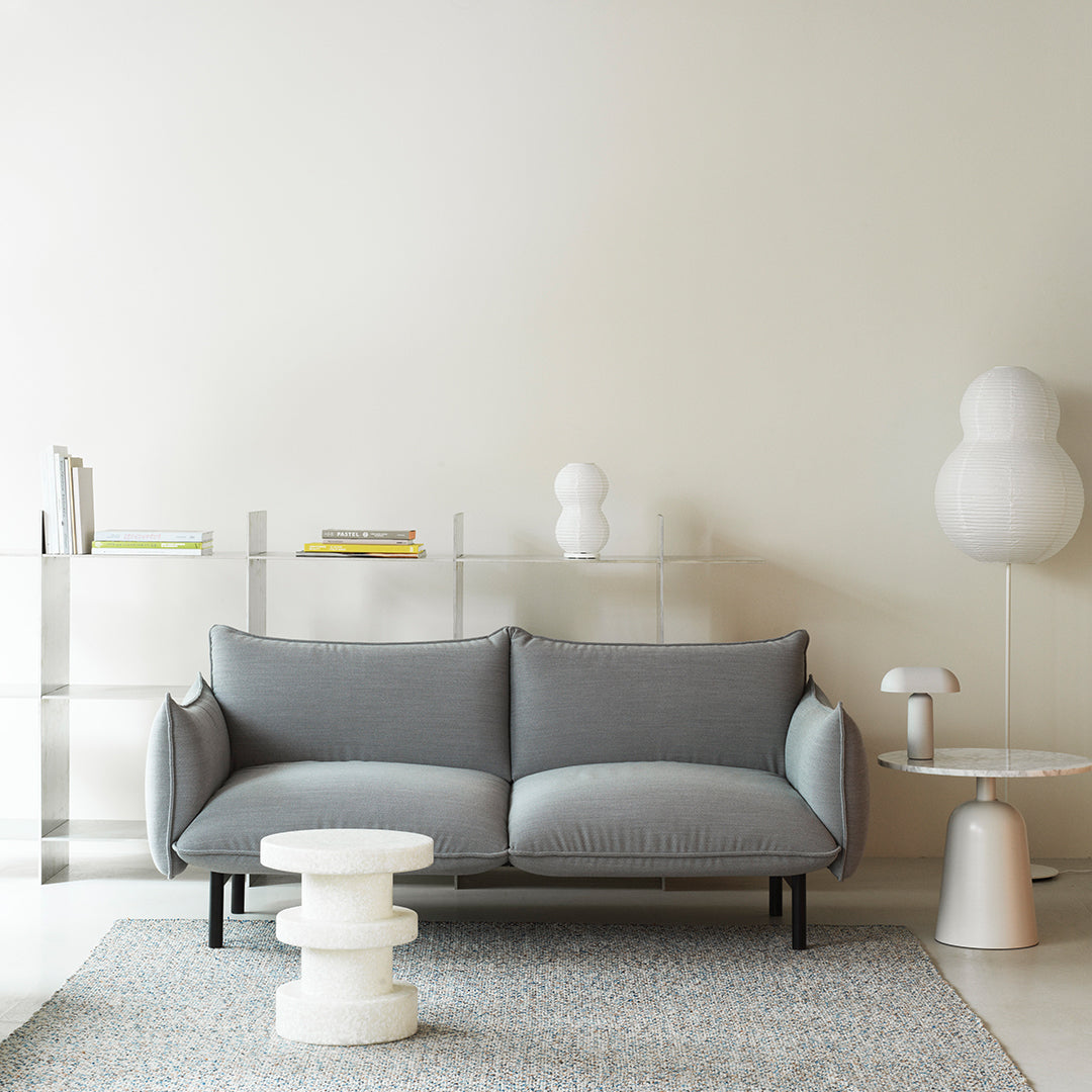 Gray modern sofa on a neutral backdrop with patterned rug and white decorative accents. Stylish minimalist aesthetic.
