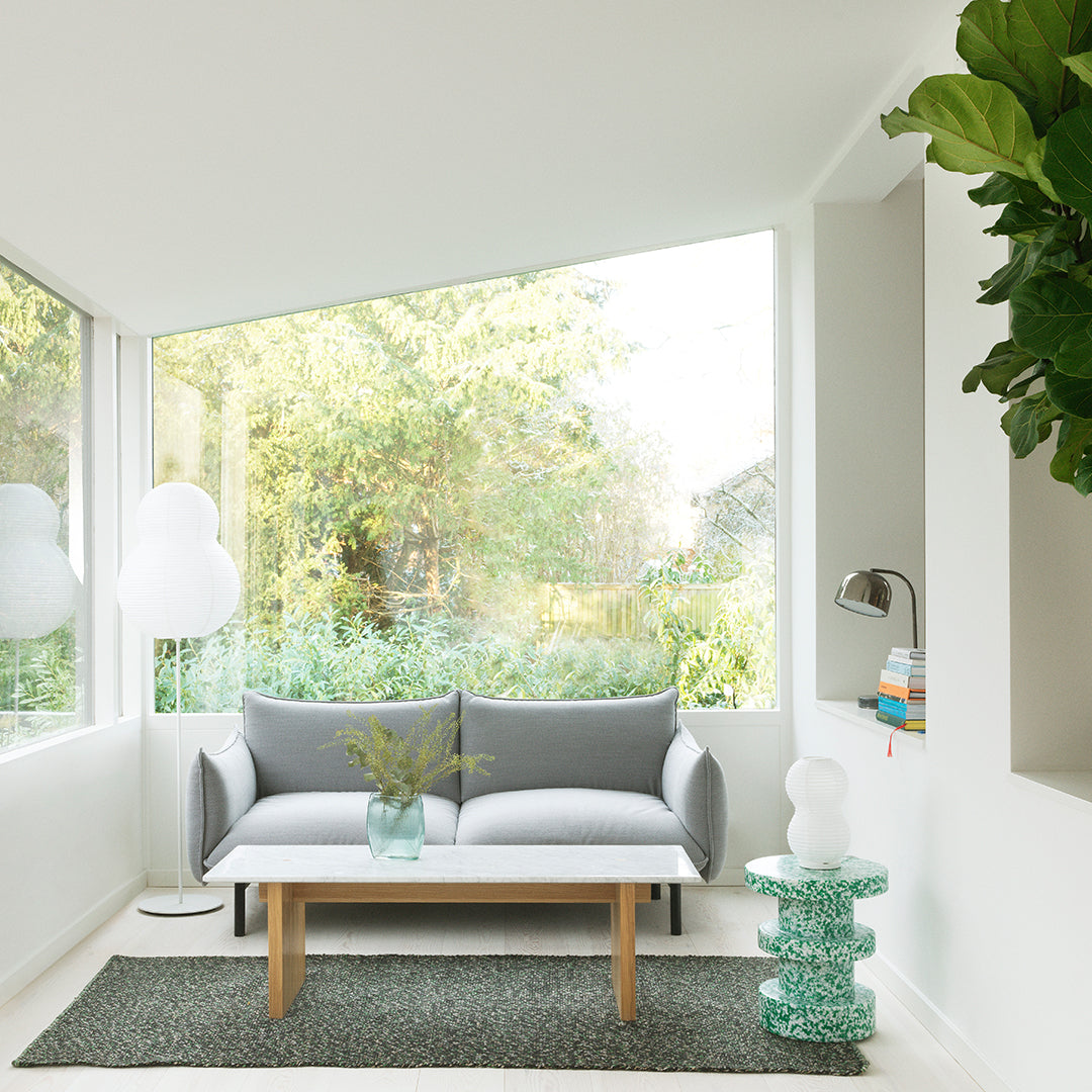 Gray sofa with white cushions, complemented by a green patterned rug and a teal decorative table. Bright, natural light ambiance.