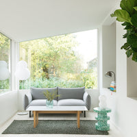 Gray sofa with white cushions, complemented by a green patterned rug and a teal decorative table. Bright, natural light ambiance.