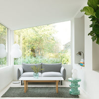 "Modern grey sofa with white cushions, green plants, and a textured dark rug in a bright, airy space."