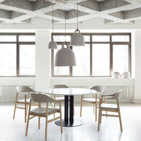 Modern dining room with a round white table, natural wood chairs, and gray pendant lights against a clean, minimal backdrop.