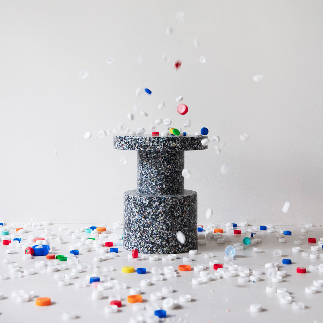 Gray speckled pedestal with colorful scattered confetti in red, blue, yellow, and white on a white background.