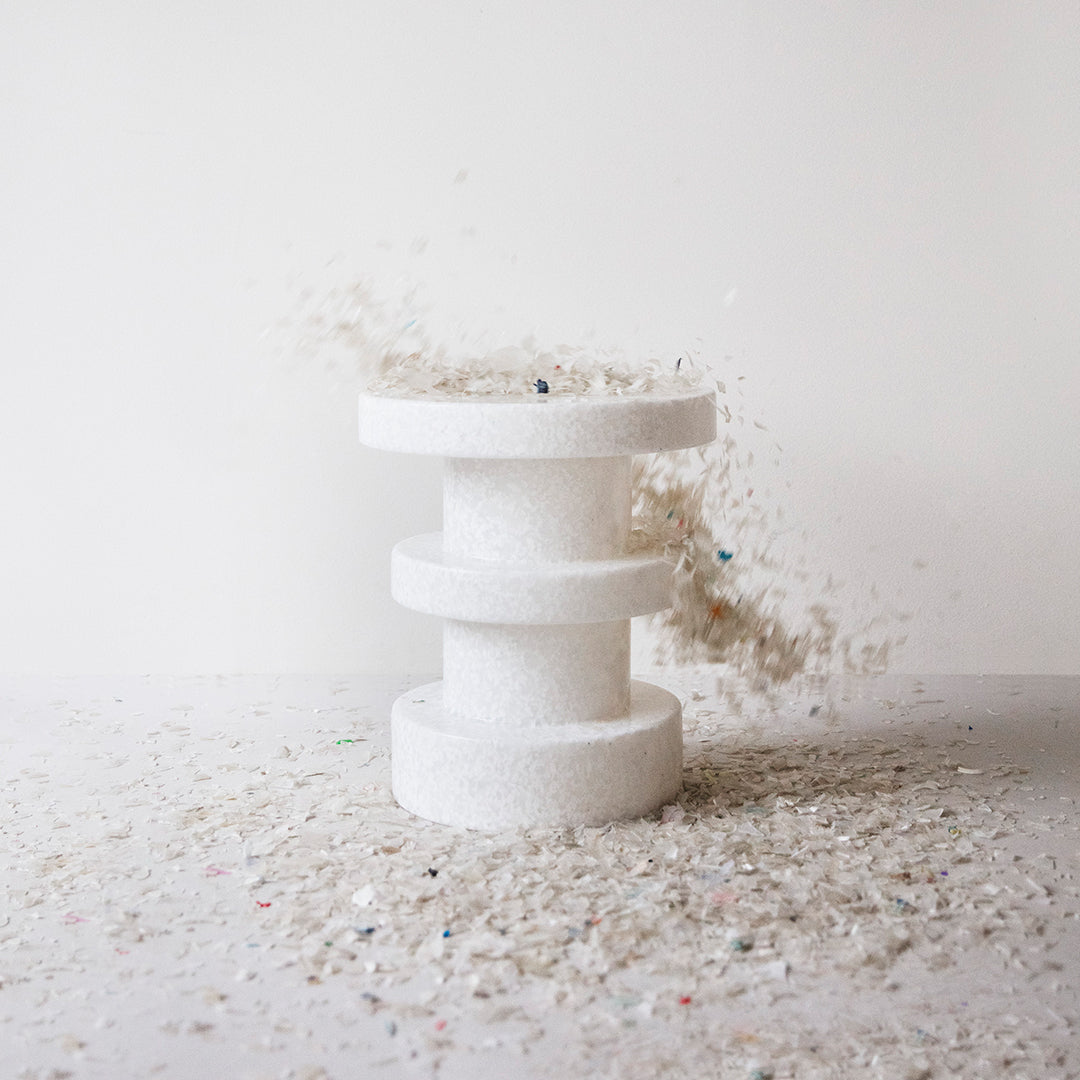 White three-tiered pedestal with a textured surface, surrounded by multicolored glitter particles.