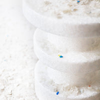 "Stacked white discs with colorful flecks on a soft white background, showcasing a minimalist and modern design."