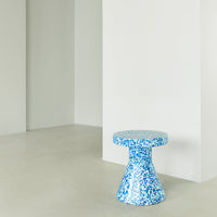 Blue speckled ceramic stool on a minimalist backdrop, featuring a unique contemporary shape and vibrant pattern.