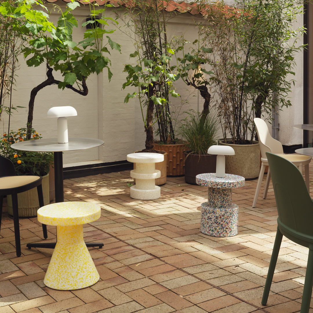 Colorful patterned stools in yellow, white, and multicolor, set in a vibrant outdoor patio with greenery.