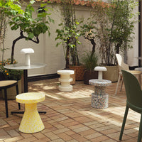 Colorful outdoor stools in yellow, white, and speckled patterns, set against a garden backdrop.