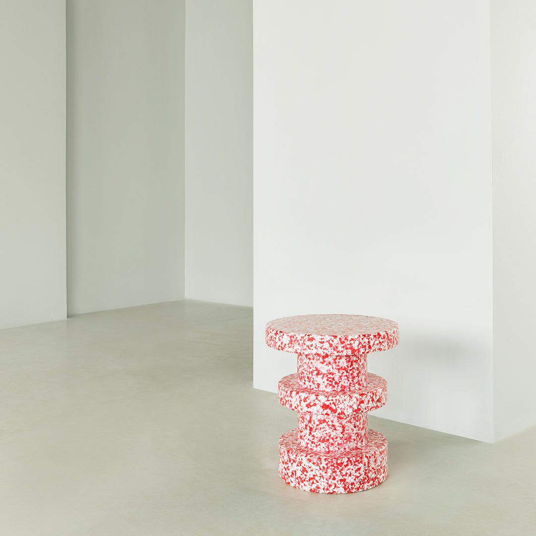 Red and white patterned three-tiered stool against a light gray wall, perfect for modern decor.