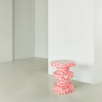 Red and white patterned three-tiered stool against a light gray wall, perfect for modern decor.