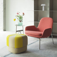 "Modern chair in coral pink with a yellow and beige striped ottoman, set against a minimalist backdrop."