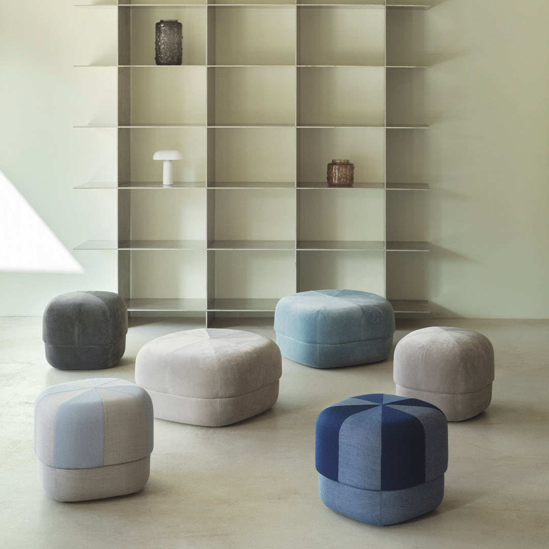 Multicolored upholstered poufs in shades of gray, blue, and cream with geometric patterns, arranged in a modern setting.