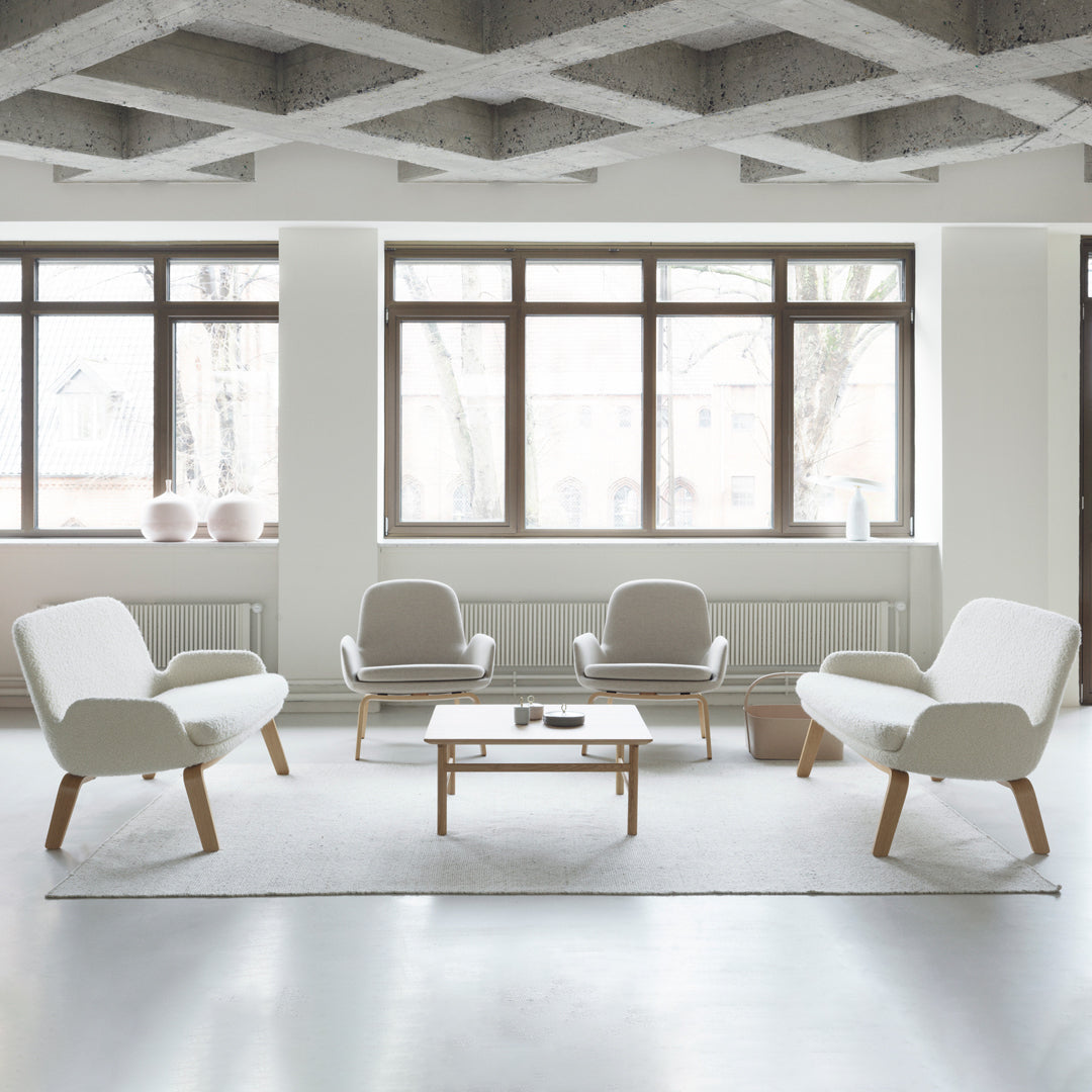 Bright white furniture with soft gray accents on a light rug, set against large windows and a textured ceiling.