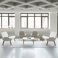 Bright white furniture with soft gray accents on a light rug, set against large windows and a textured ceiling.