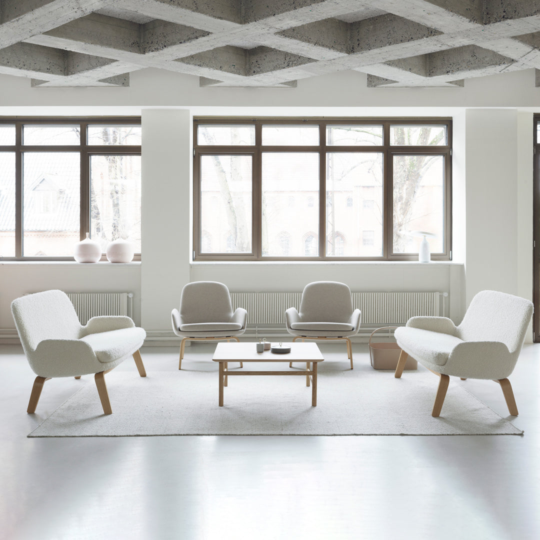 Minimalist white chairs with wooden legs in a modern, gray-patterned room featuring large windows and natural light.
