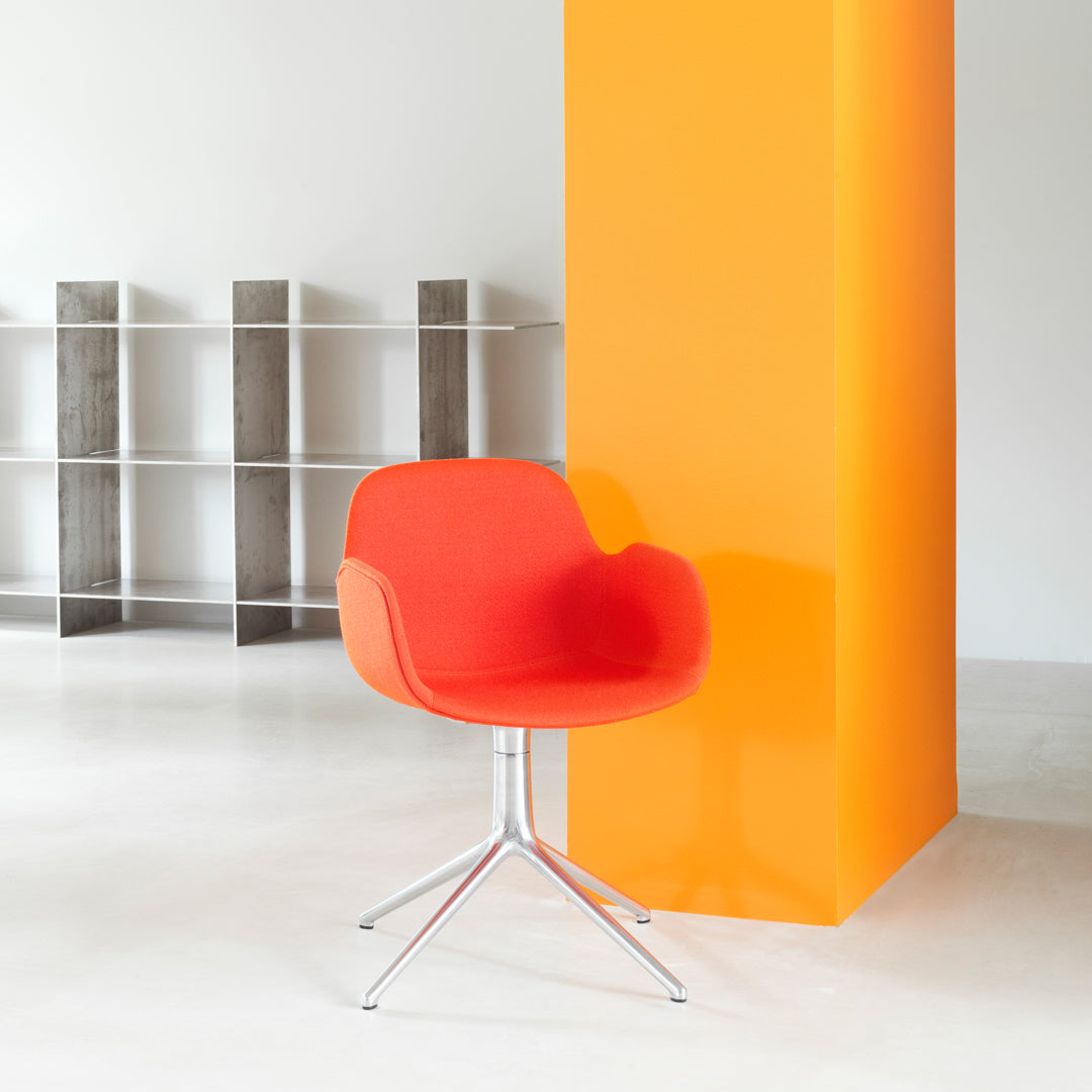 Bright red modern chair with smooth upholstery, set against a vibrant orange wall, showcasing a minimalist design.