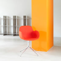 Bright red modern chair with smooth upholstery, set against a vibrant orange wall, showcasing a minimalist design.