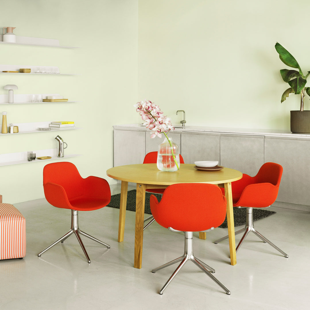 Bright red chairs around a wooden table in a light green room with a minimalist design and potted plant accents.
