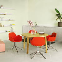 Bright red chairs around a wooden table in a light green room with a minimalist design and potted plant accents.