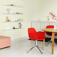 Bright red chair and soft pink sofa against a light yellow wall, featuring minimalist white shelves and a wooden table.