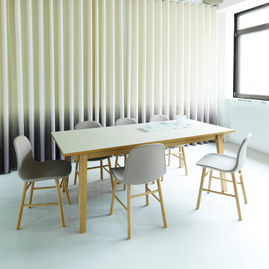 Modern dining table with pale wood legs and neutral gray chairs against soft beige and gray vertical striped backdrop.