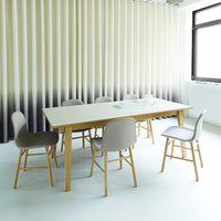 Modern dining table with pale wood legs and neutral gray chairs against soft beige and gray vertical striped backdrop.